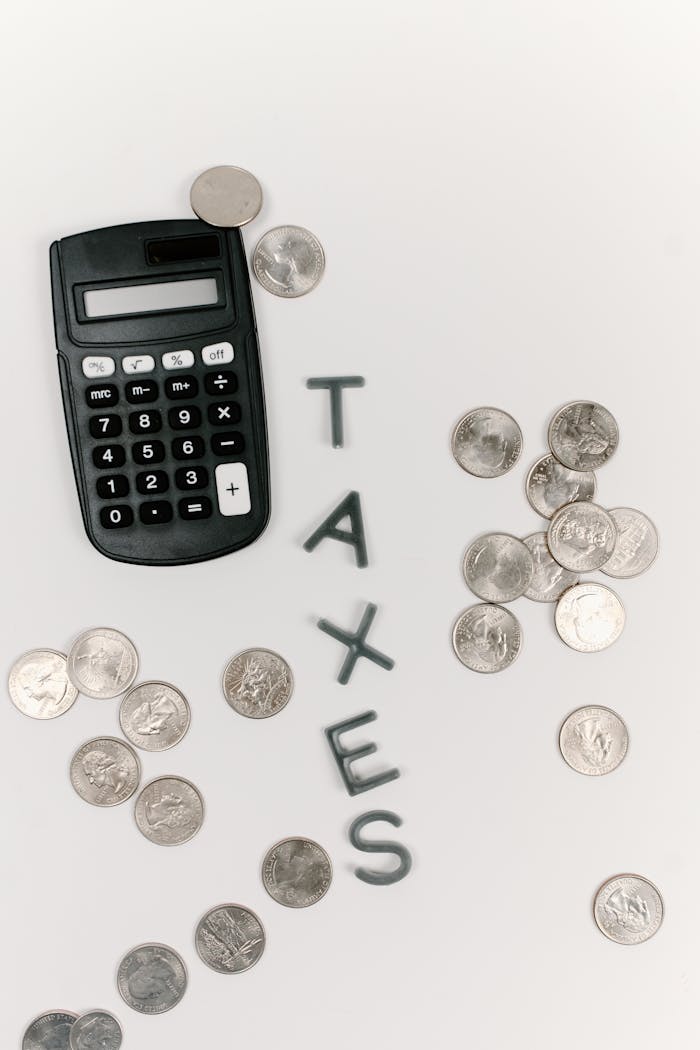 our-story-02 Calculator and scattered coins with the word 'TAXES' on a white background.